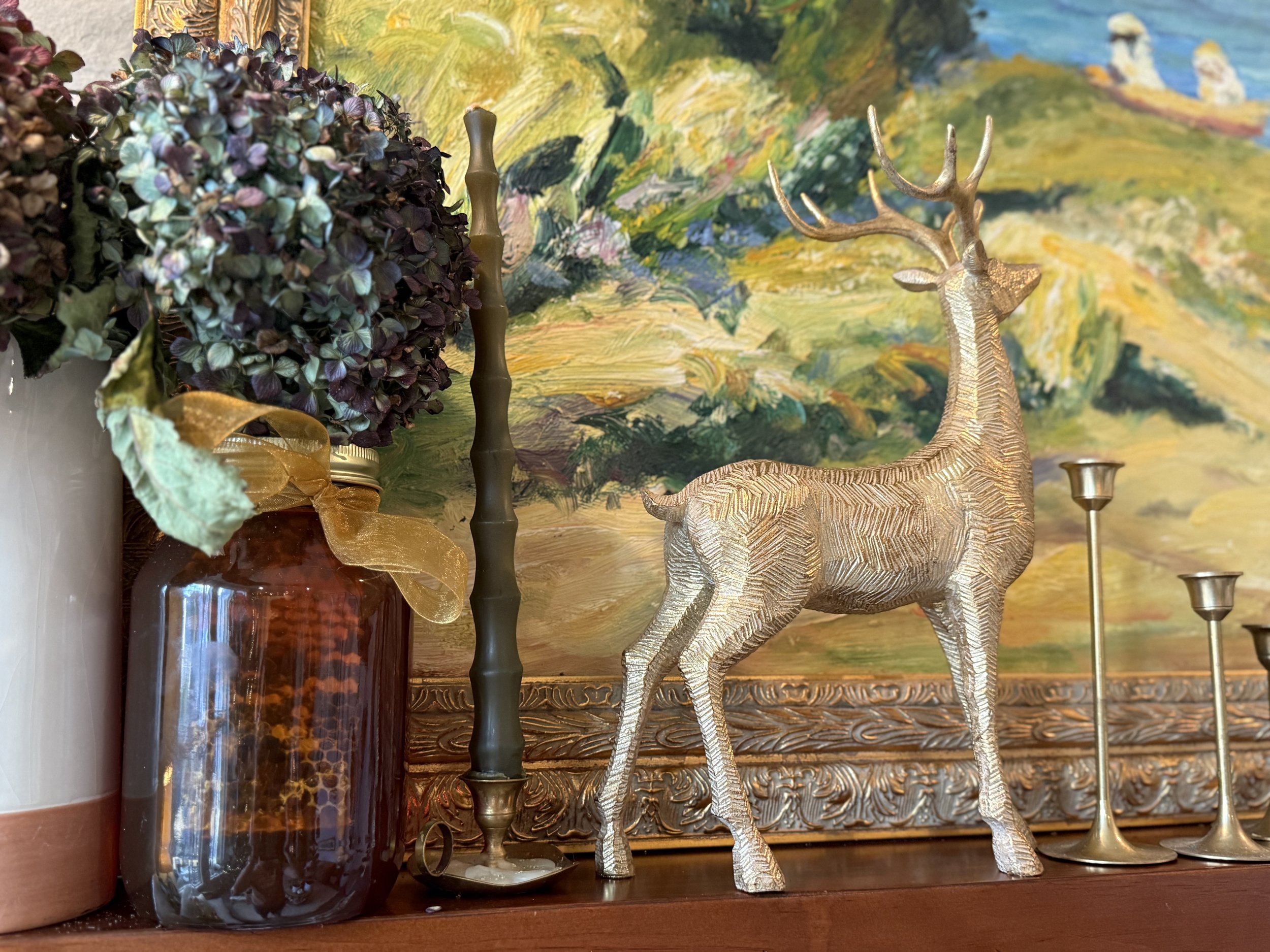 A golden deer sculpture beside dried flowers and a colorful painting
